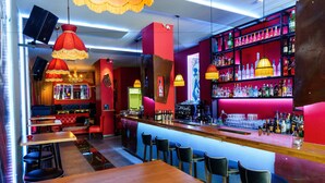 Un bar con mesas de madera y taburetes negros, paredes rojas y estanterías llenas de botellas.