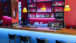 Un bar con varias estanterías llenas de botellas de licores, taburetes y lámparas colgantes.