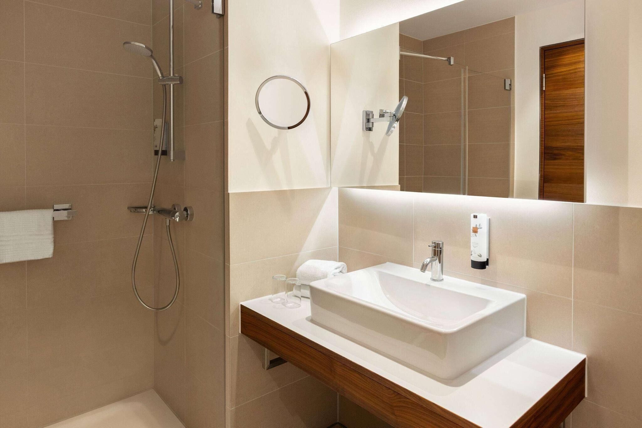 A modern bathroom with a large sink, a mirror, a shower, and a towel rack.