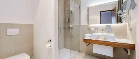 A modern bathroom with a glass-enclosed shower, a white toilet, and a vanity with a mirror and towel rack.