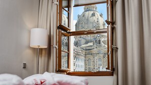 Quarto de hotel com uma grande janela que oferece vista para um edifício histórico com cúpula e arquitetura elaborada.