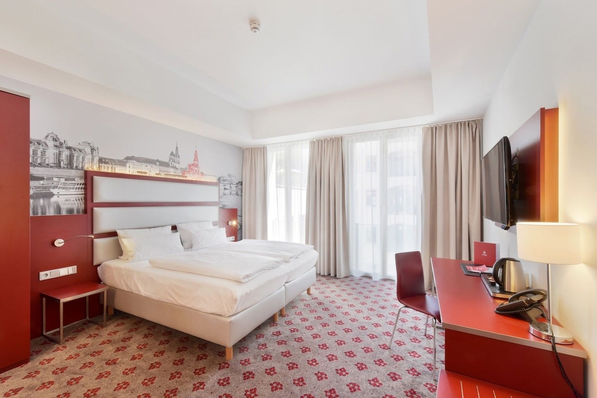A hotel room with a bed, a desk, a chair, a television, and a window with curtains.