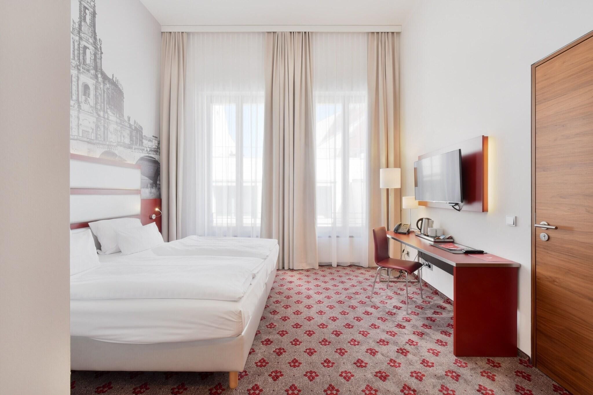 Ein Hotelzimmer mit einem Bett, einem Schreibtisch mit Stuhl, einem Fernseher und einer Tür.