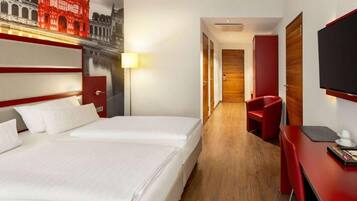 A hotel room with two beds, a desk, a chair, a TV, and a mural of a building.