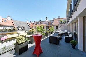 Terraço no telhado com área de estar externa, plantas em vasos e uma mesa vermelha.