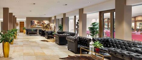 A spacious lobby with leather sofas, a central art piece, and potted plants.