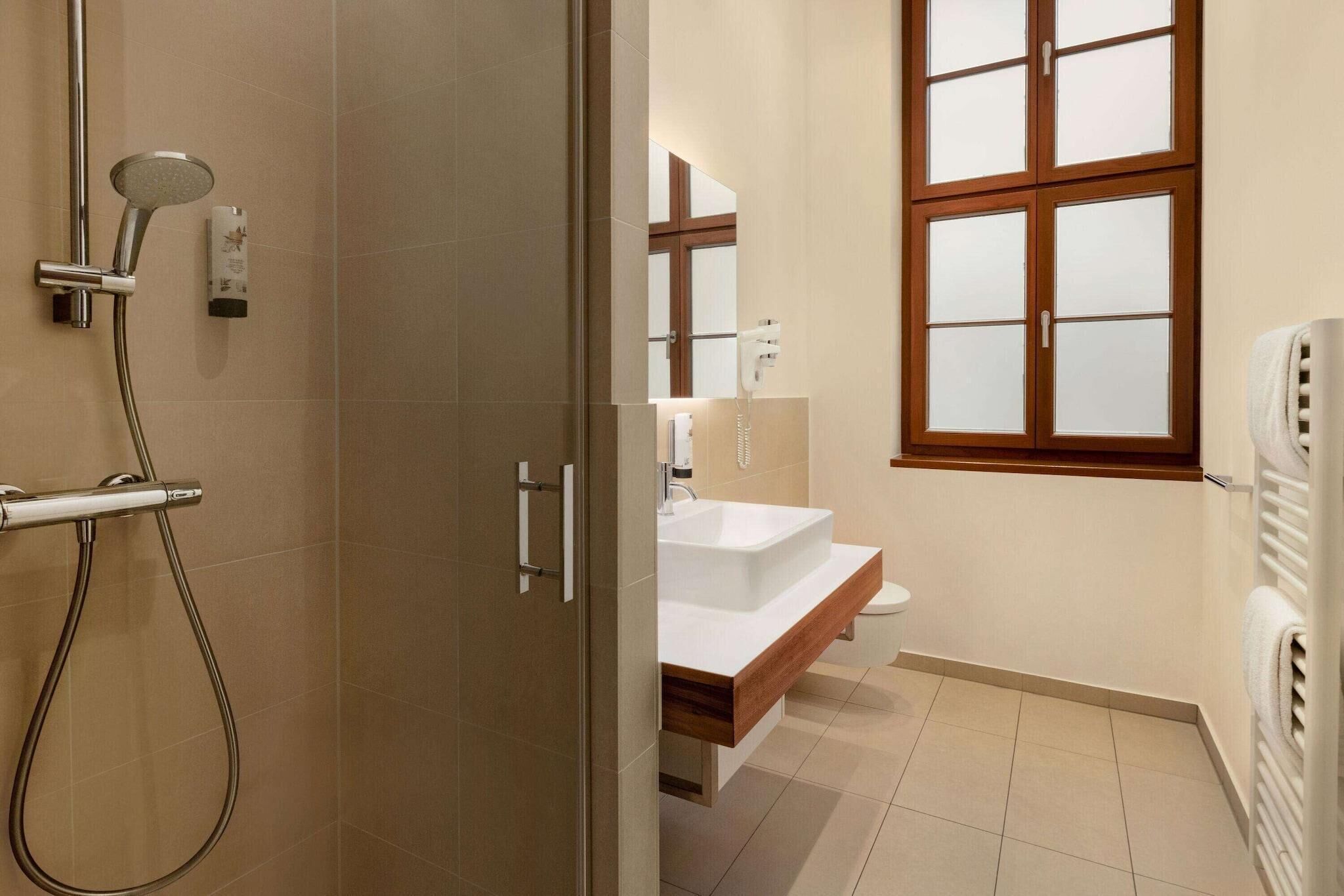 Un baño con ducha, inodoro, lavamanos y una ventana con vidrio esmerilado.