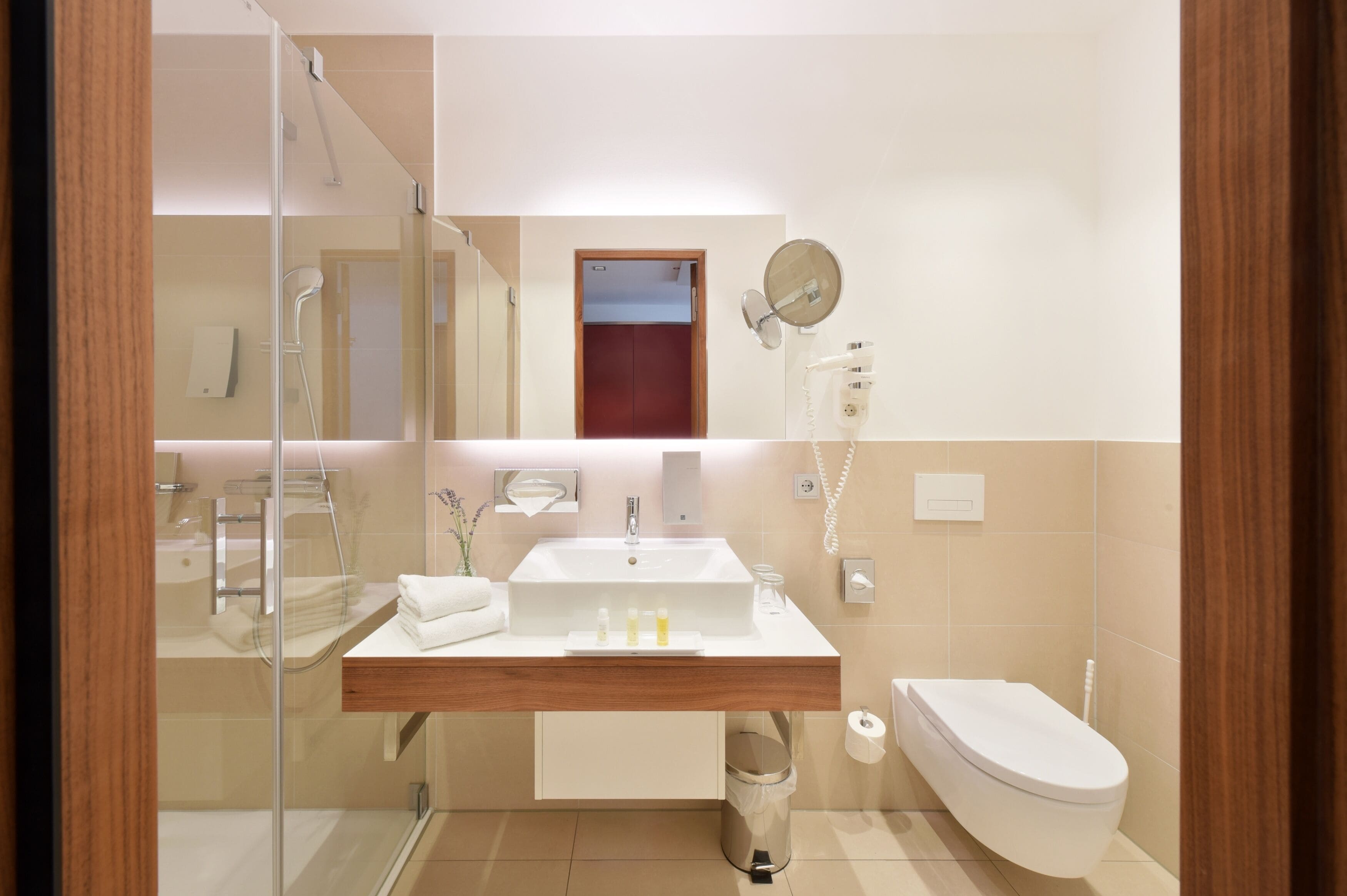 Un baño moderno con cabina de ducha de vidrio, un lavamanos blanco con encimera de madera, un espejo y un inodoro.