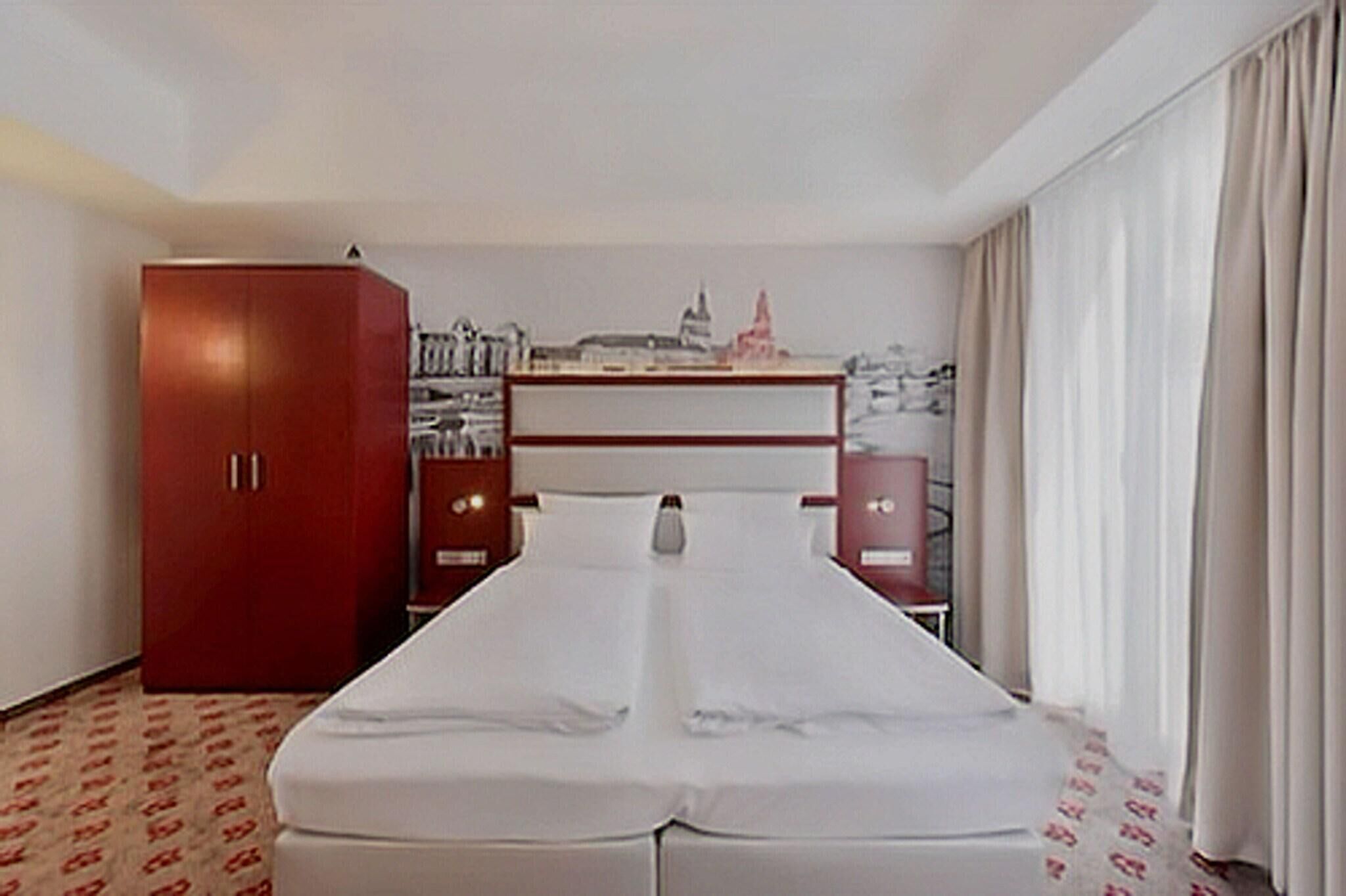 Ein Hotelzimmer mit einem Bett, einem Kleiderschrank, einem Schreibtisch und einem an der Wand befestigten Regal.