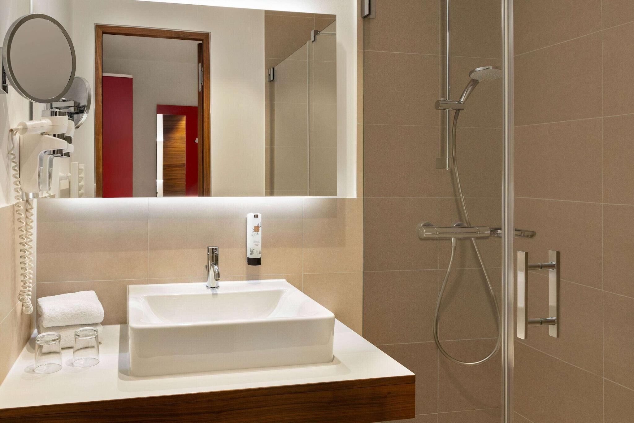 Une salle de bain moderne avec un grand miroir, un lavabo rectangulaire, une douchette à main et un porte-serviettes.