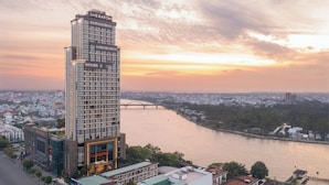 A high-rise hotel with a modern glass facade, situated by a river with a bridge in the background.