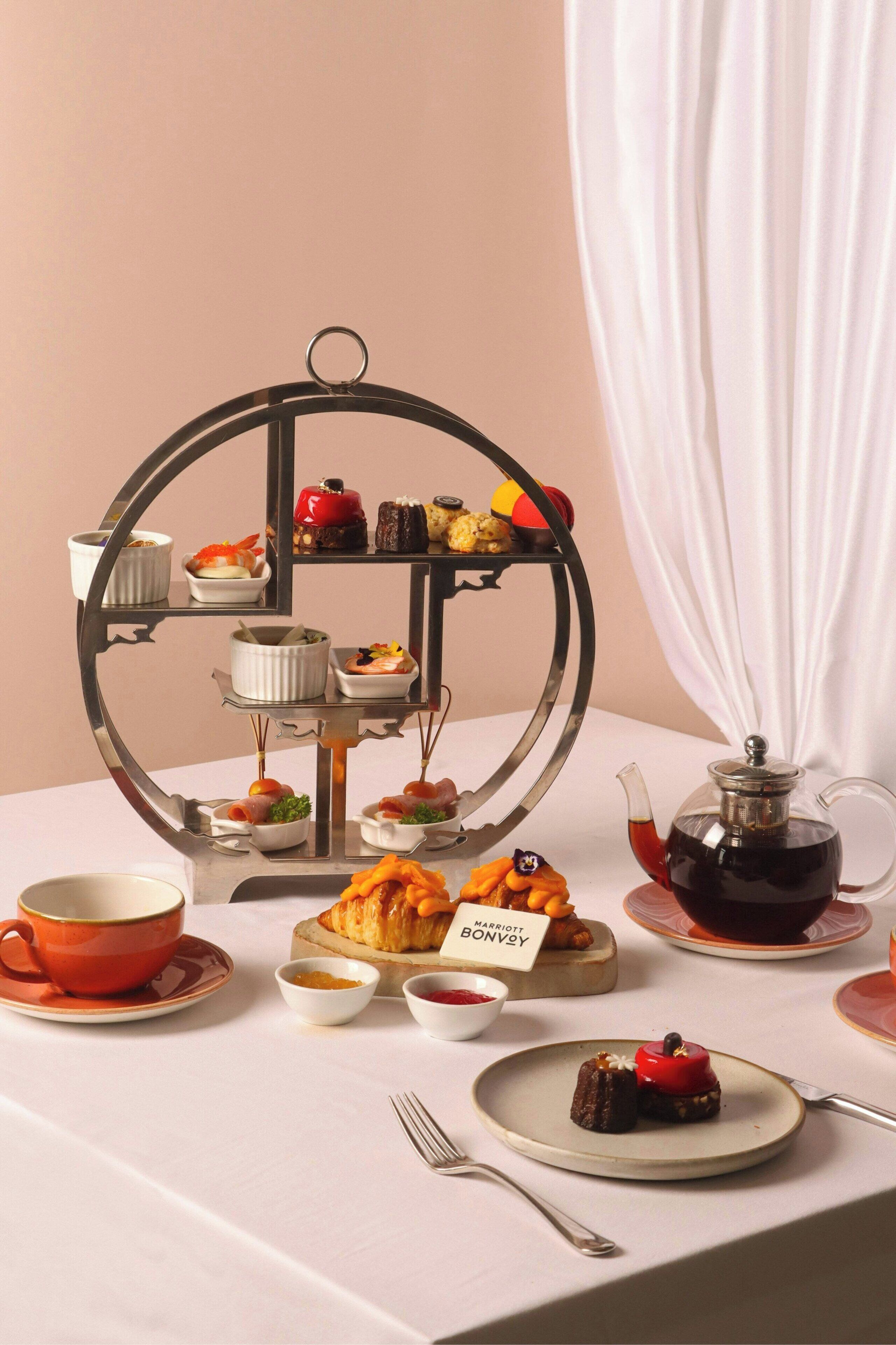 A three-tiered dessert display with various pastries and a teapot on a table.
