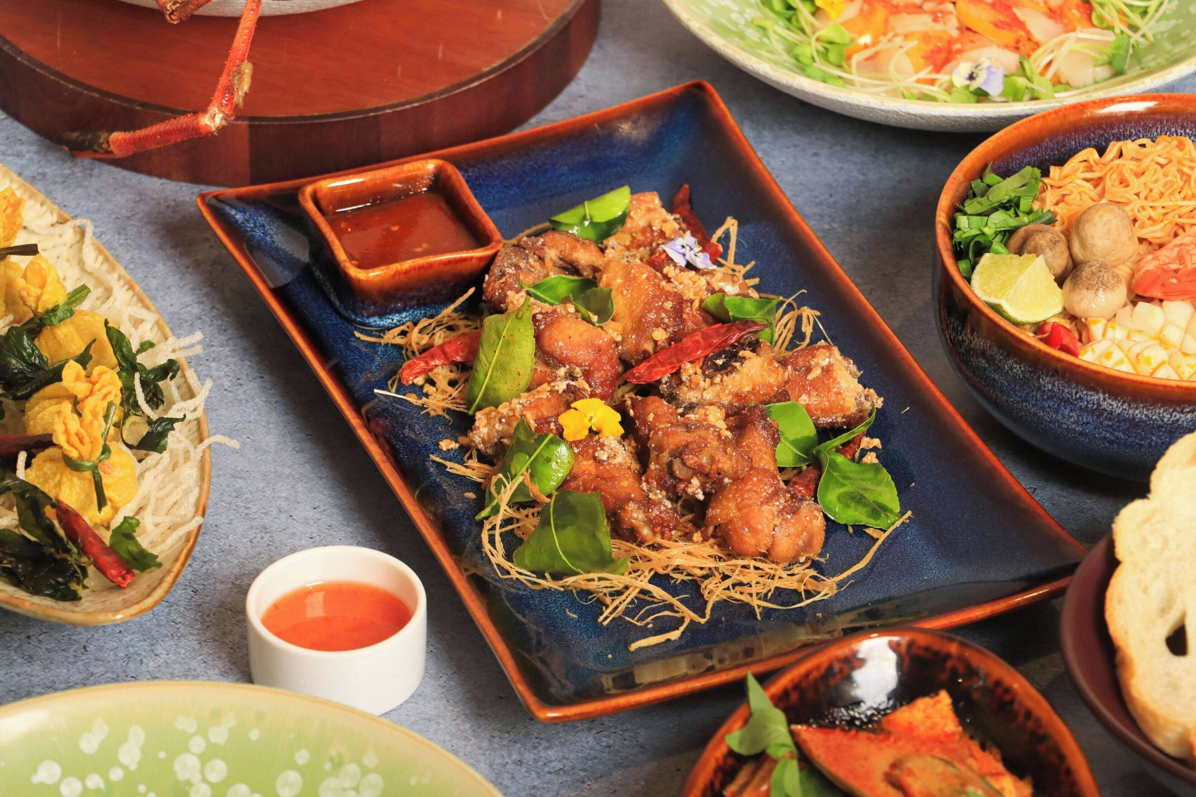 A variety of dishes including fried chicken, noodles, and salads, served on different plates and bowls.