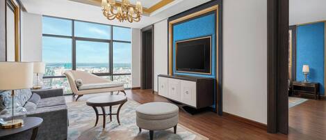 Una sala de estar moderna con un sofá, un reposapiés y una mesa de centro, un televisor montado en la pared y un amplio ventanal con vistas a la ciudad.