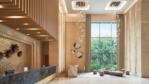 A modern lobby with a reception desk, seating area, and large windows offering a view of greenery.