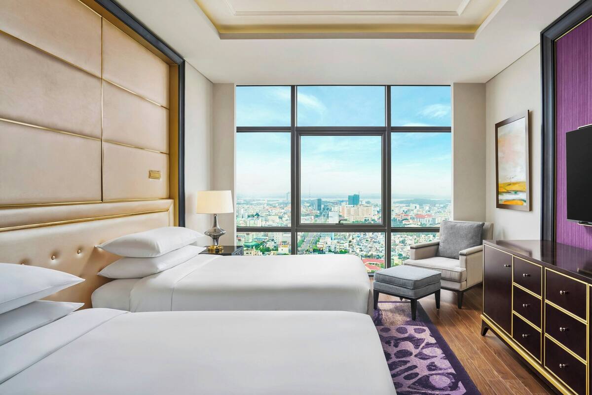 Habitación de hotel con dos camas, vistas a la ciudad, televisión y diseño moderno.
