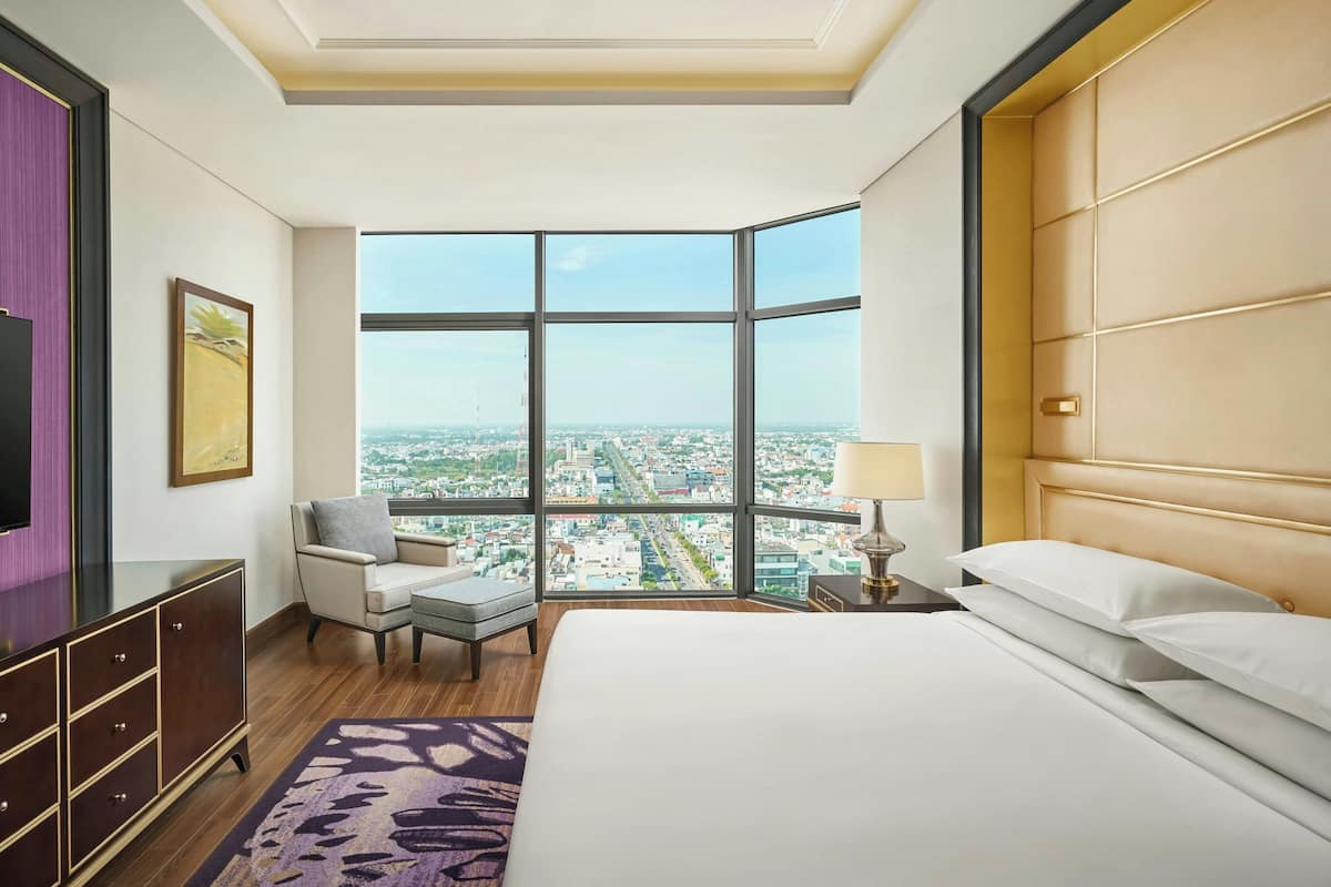 Habitación de hotel con un ventanal grande que ofrece vistas a la ciudad, una cama, un escritorio y una silla.