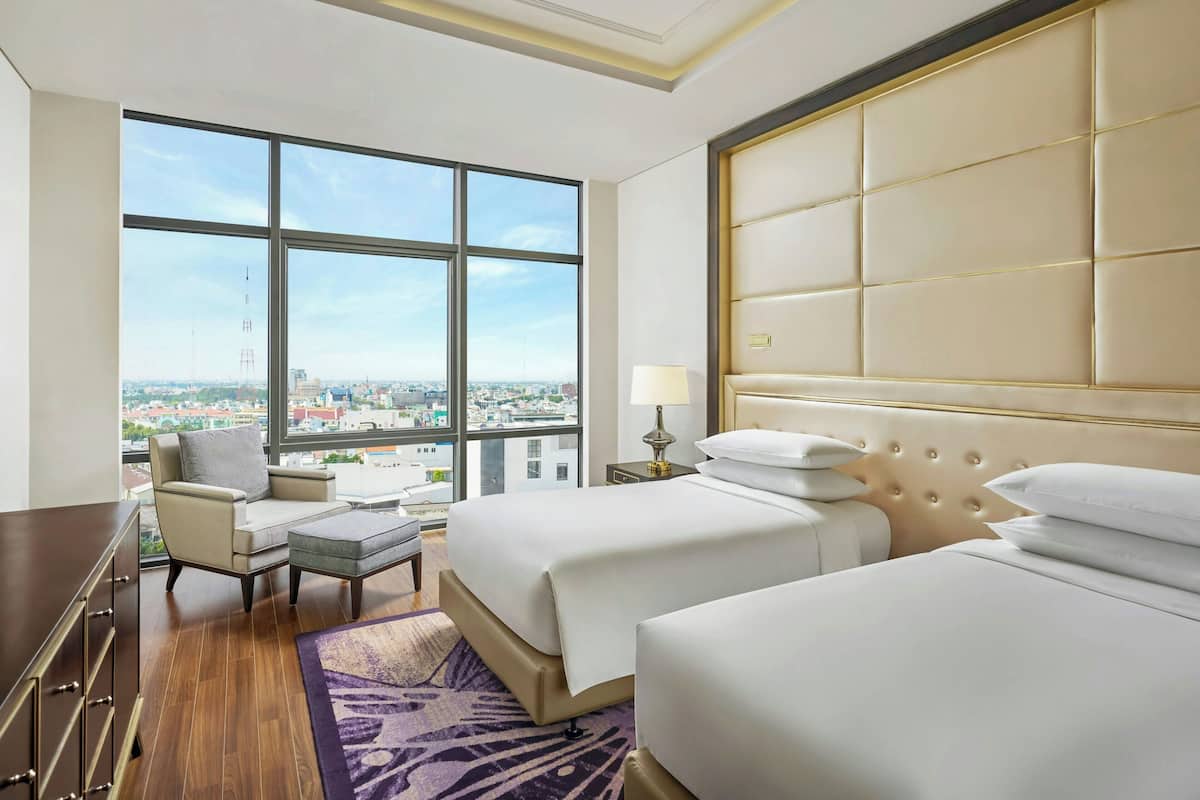 Habitación de hotel con un ventanal grande, dos camas, un escritorio y una silla.