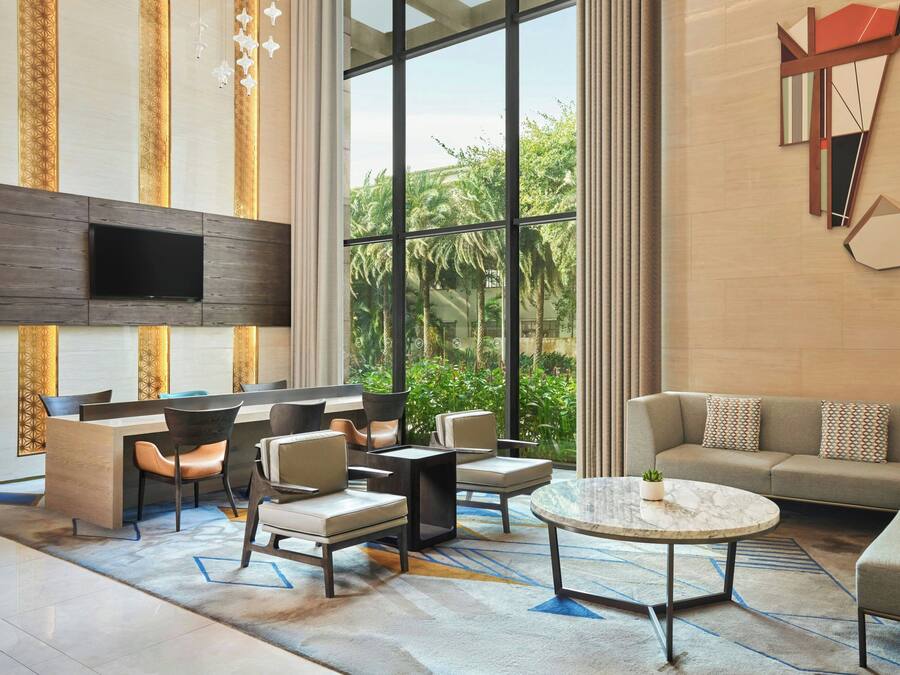 Una sala de estar moderna con un televisor de pantalla plana, asientos cómodos, una mesa de centro y ventanas amplias con vistas a zonas verdes.