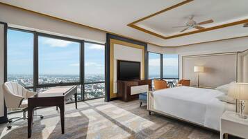 A hotel room with a large bed, a desk, a chair, a TV, and a view of the city.