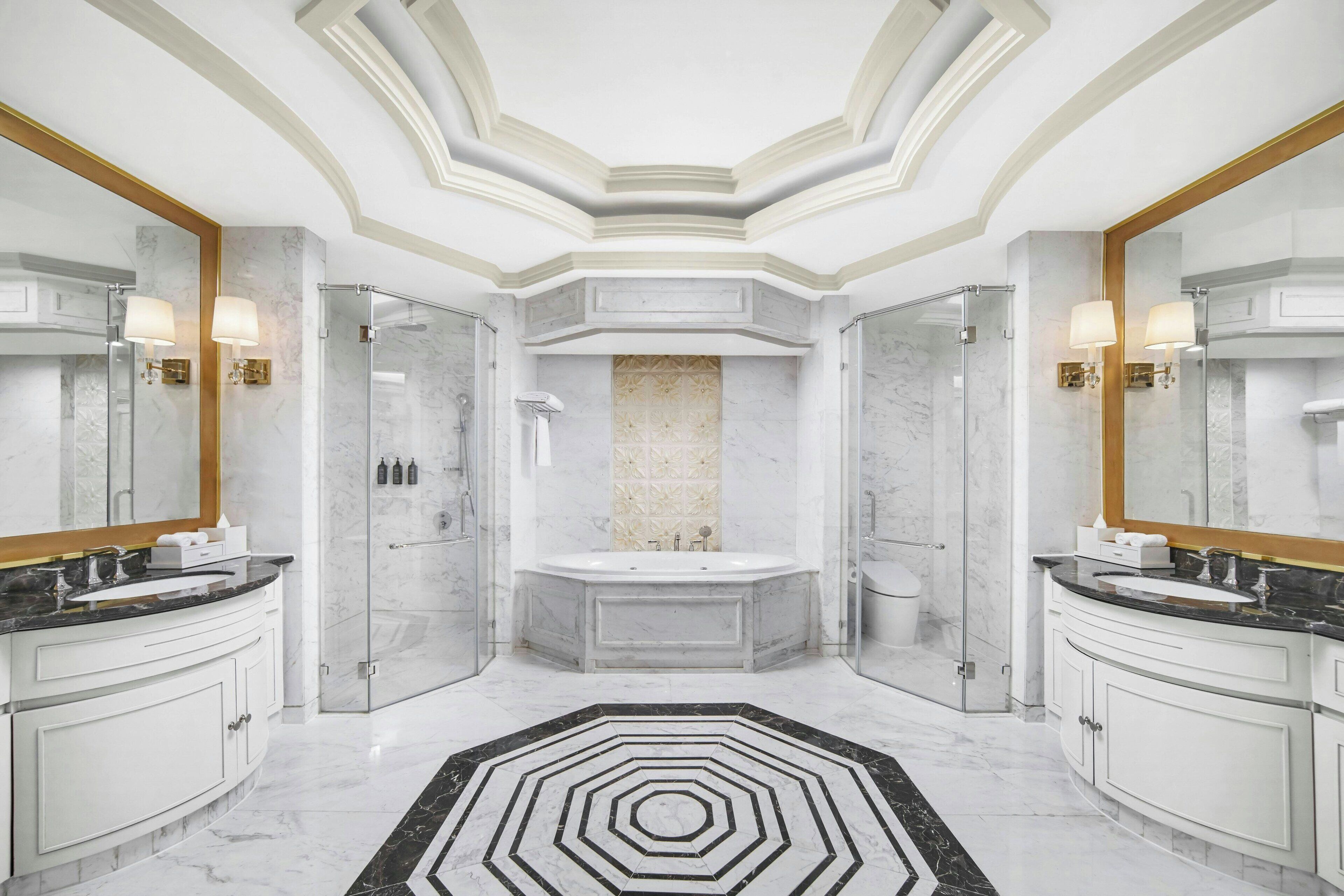 A luxurious bathroom with a central bathtub, two sinks, and a black and white patterned floor.