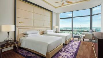 Habitación de hotel con dos camas, un ventanal amplio con vistas a la ciudad, un ventilador de techo y un escritorio con lámpara.