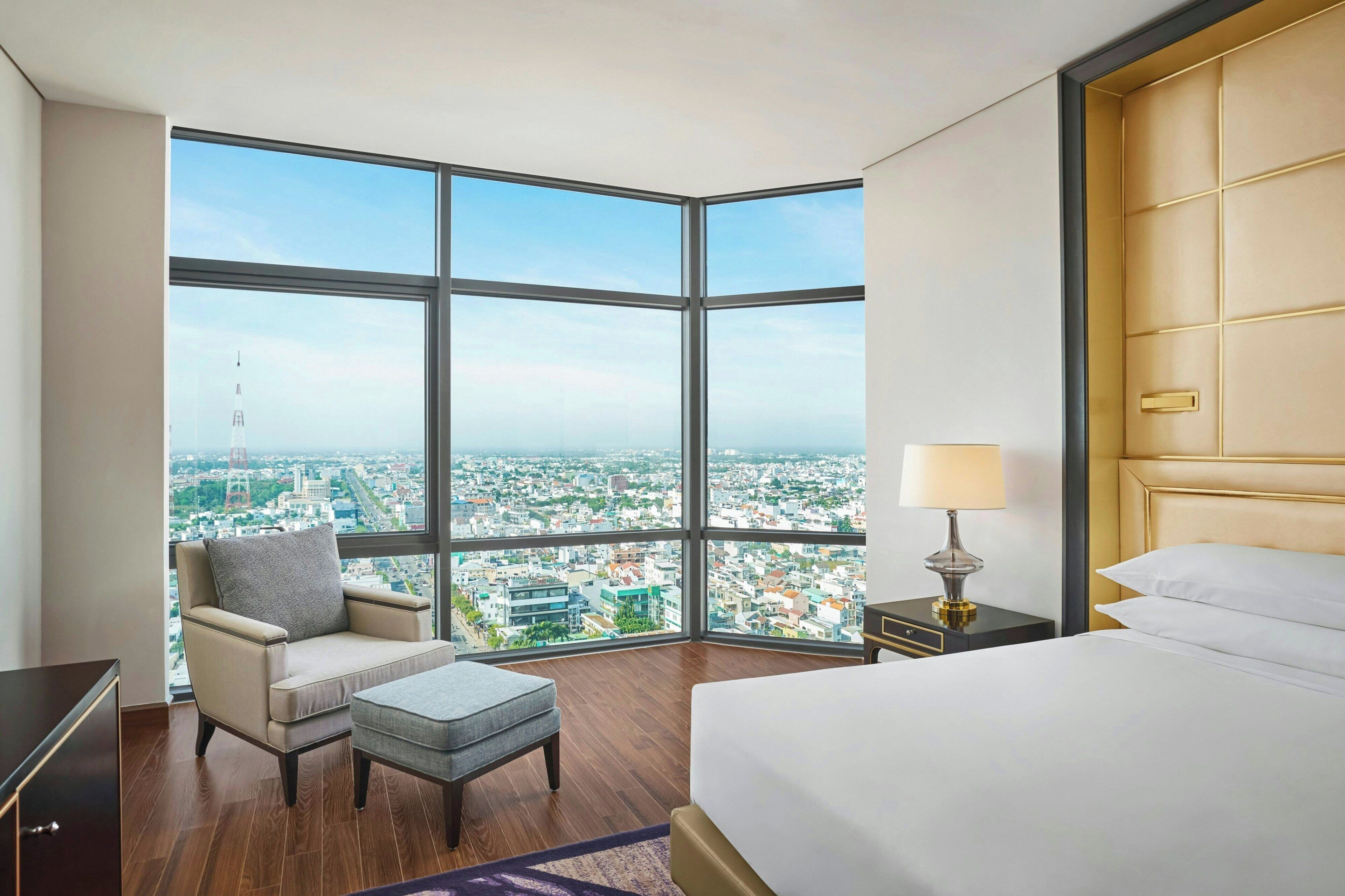 A hotel room with a large window, a bed, a chair, a nightstand, and a lamp.