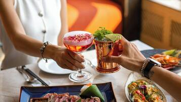 A dining table with a plate of sliced meat, a cocktail, and a glass of a beverage with a garnish.