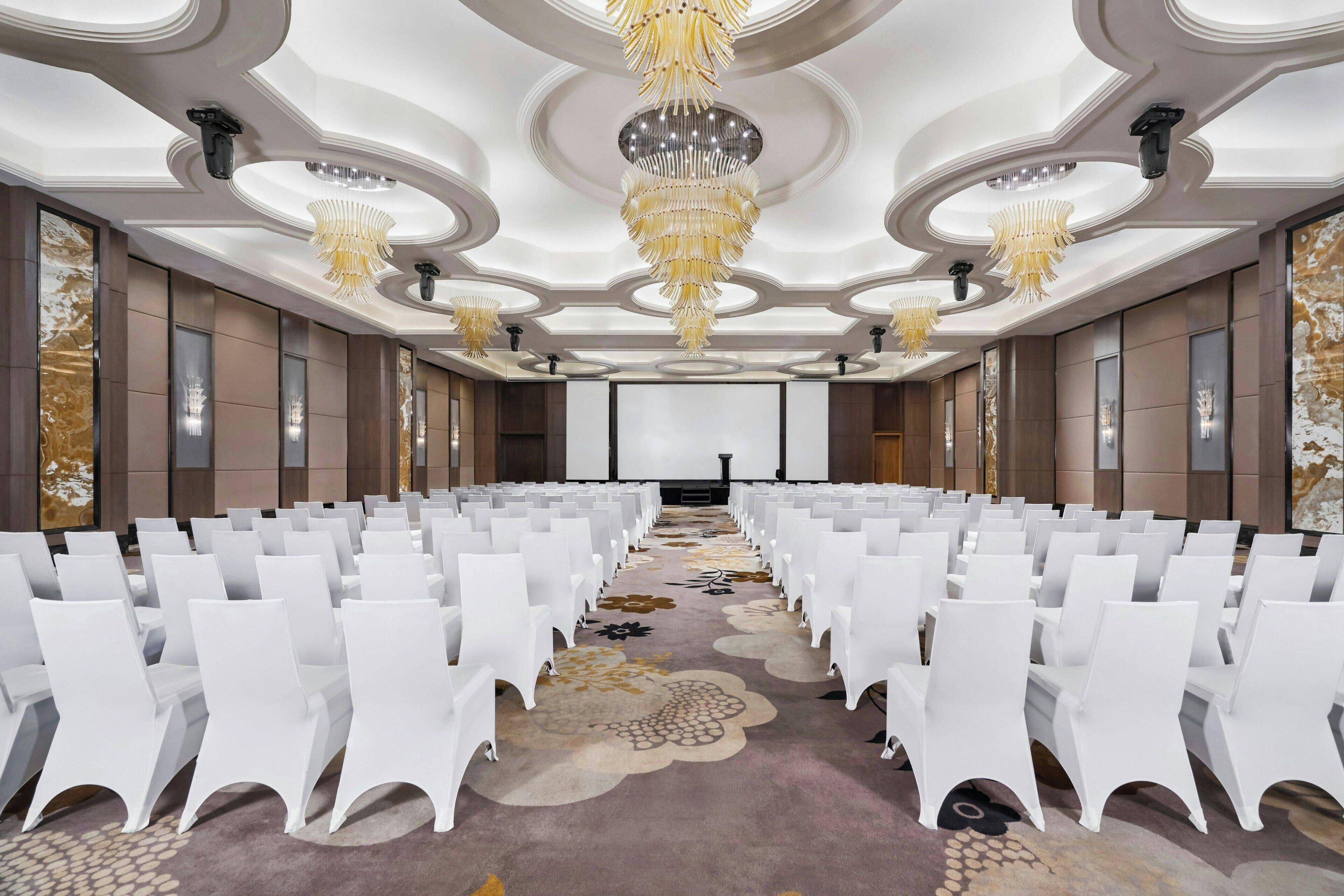 Ein Konferenzraum mit Reihen weißer Stühle, Teppichboden und einer Chandelüster.