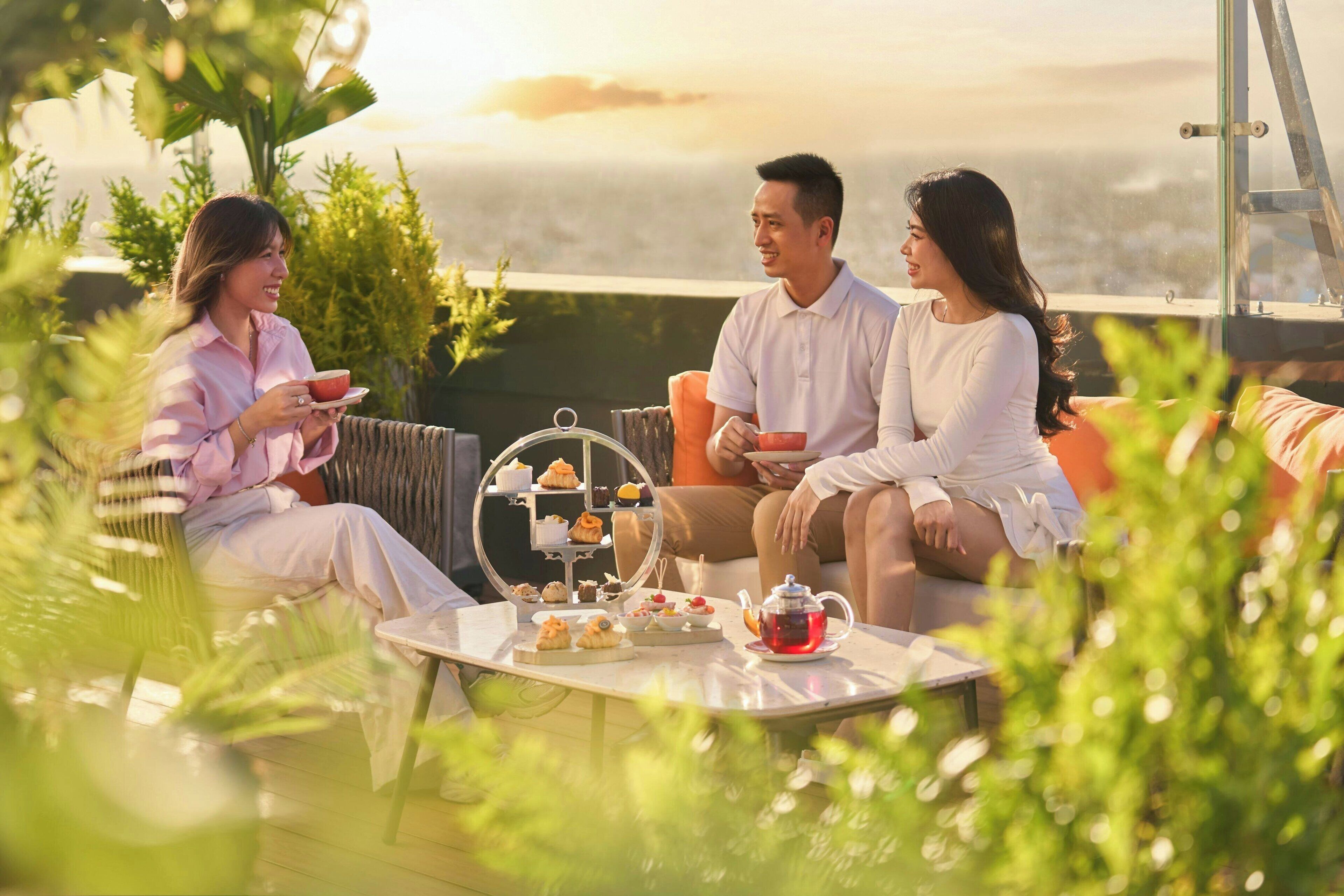 A terrace with a table set for a tea service, surrounded by greenery and overlooking a scenic view.