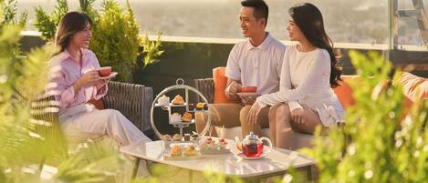 A terrace with a table set for a tea service, surrounded by greenery and overlooking a scenic view.