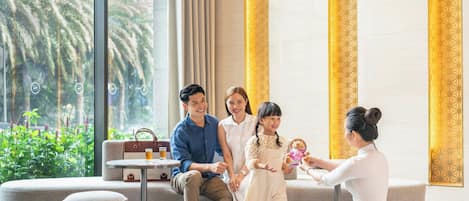 Una familia en un vestíbulo moderno con un ventanal grande, asientos cómodos y una pequeña mesa con una bebida.