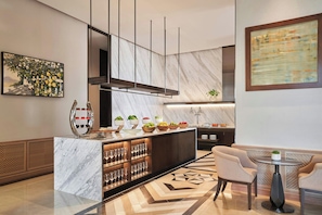 A modern kitchen with marble countertops, a central island with fruit bowls, and a bar area with glasses.