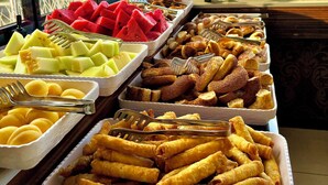 Un bufé con diversas opciones de comida, entre ellas frutas, pasteles y aperitivos fritos.