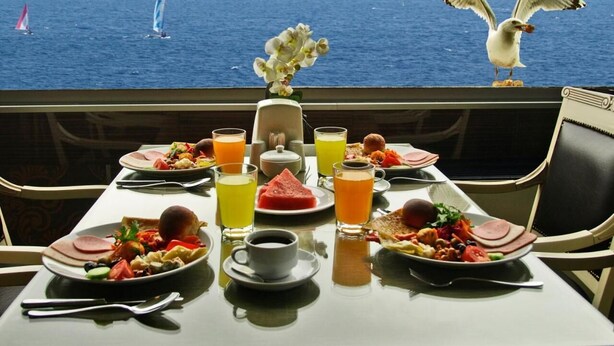 Una mesa dispuesta para el desayuno con vista al océano y veleros.