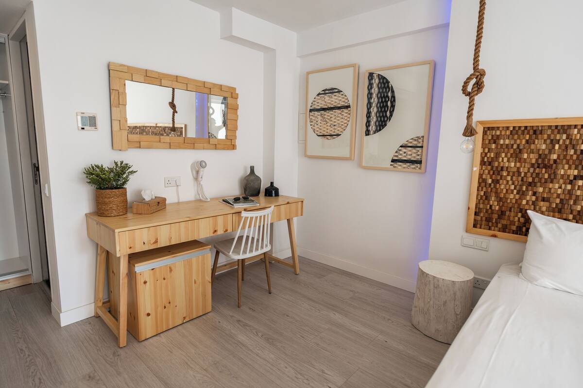 A modern bedroom with a wooden desk, a white chair, a bed with white bedding, and two framed artworks on the wall.