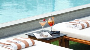 A poolside lounge area with sun loungers, a table with drinks, and a pool in the background. - Blue Harbour Boutique (Ayia Napa)