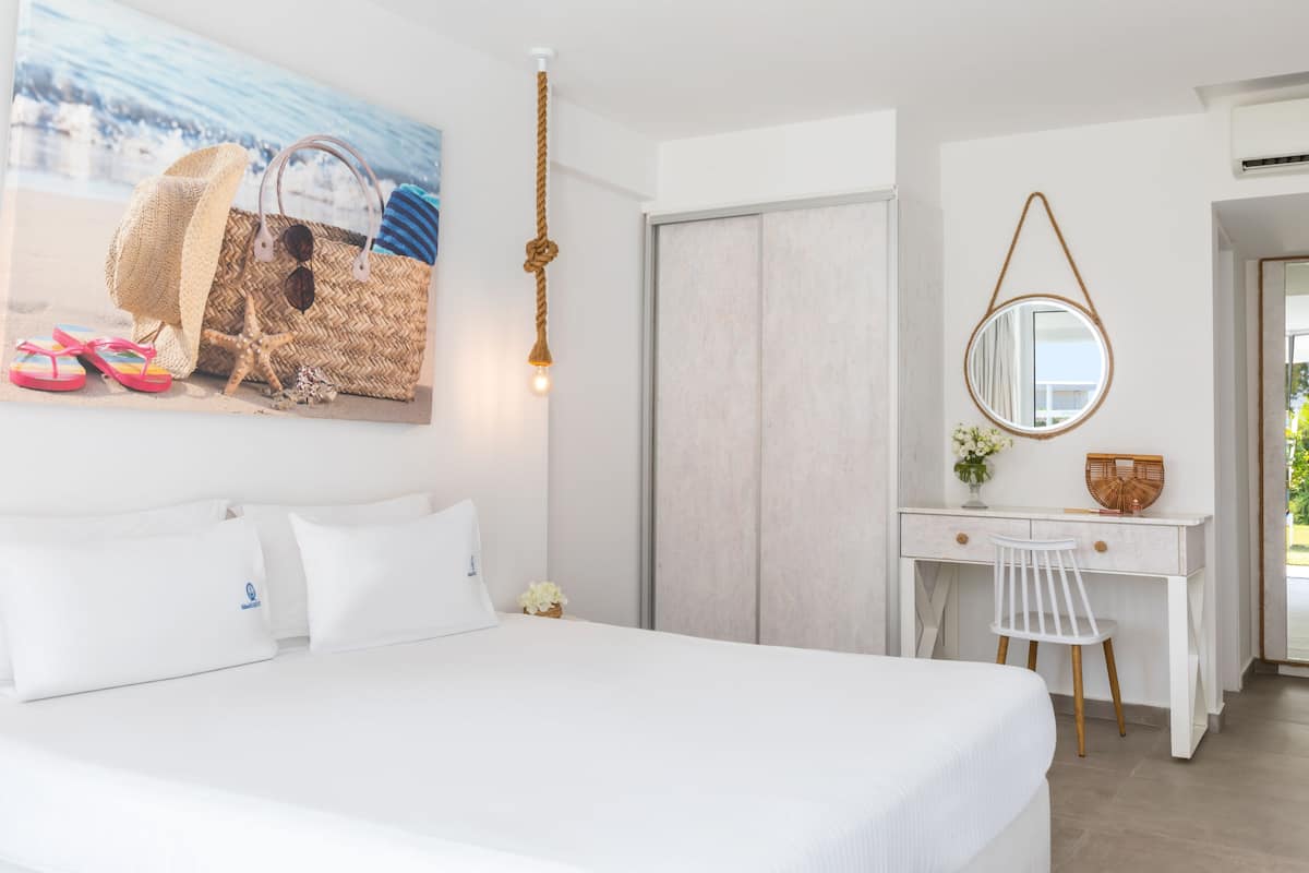 A bedroom with a bed, a desk, a chair, a hanging light, a mirror, and a painting of beach items.