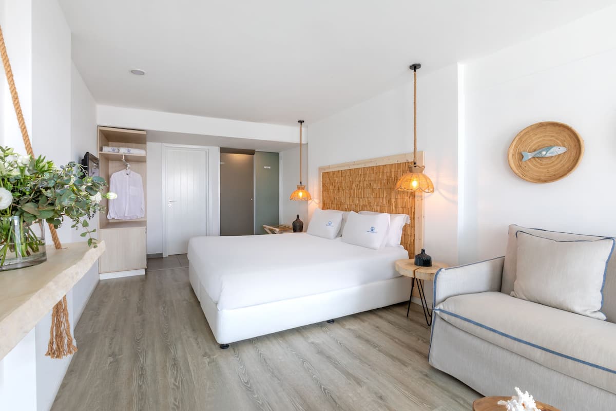 A modern bedroom with a large bed, bedside tables, a sofa, and a hanging light fixture.