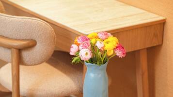 A small wooden table with two white cups of coffee, a vase with colorful flowers, and a magazine.