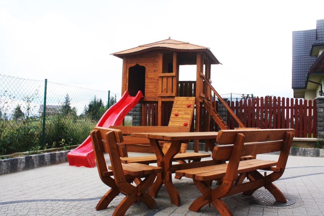 Estructura de juego de madera con tobogán y zona de escalada, rodeada de una mesa de picnic y bancos.