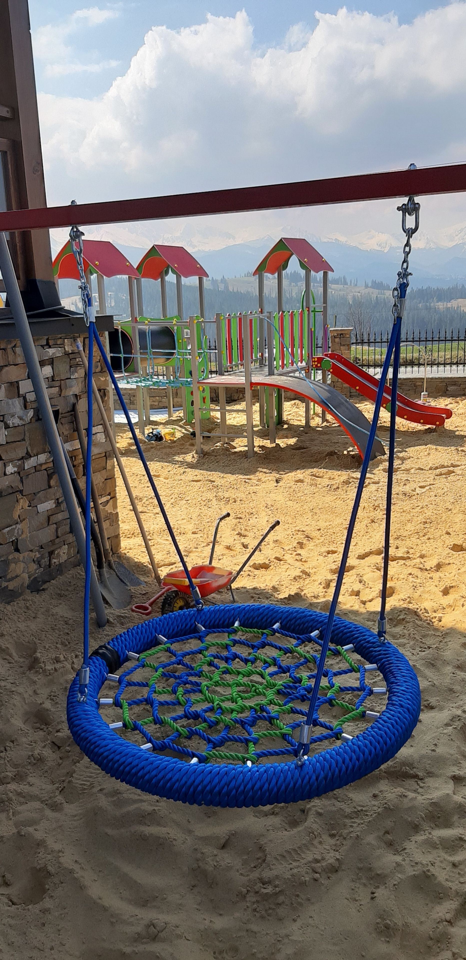 A playground with a swing set and a rope swing, set against a backdrop of mountains and a clear sky.