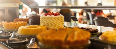 Un bufé con diversos postres, entre ellos pasteles y tartas, expuestos en un mostrador de vidrio.