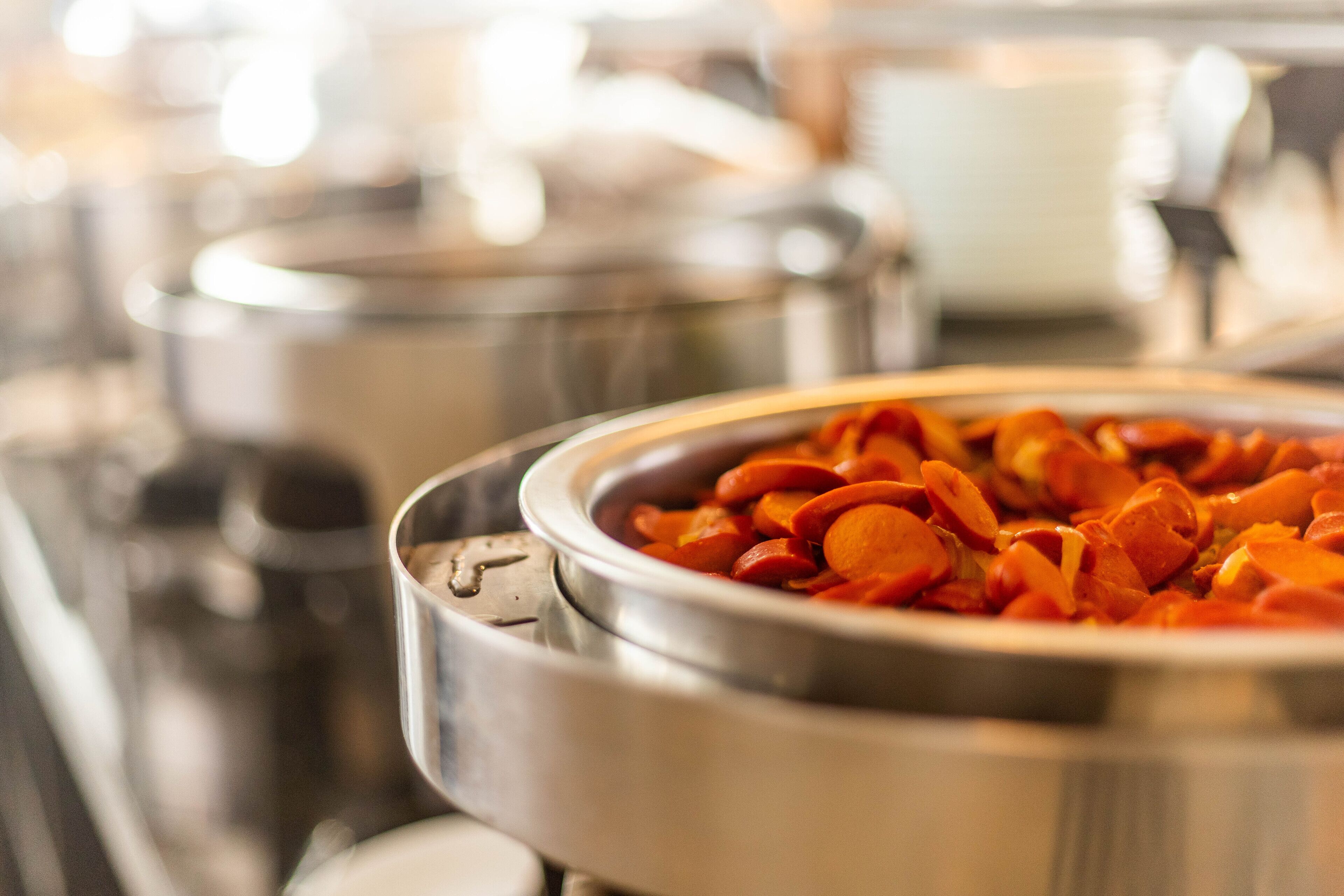 Un bufé con distintos alimentos, incluyendo zanahorias en rodajas, presentados en recipientes de acero inoxidable.