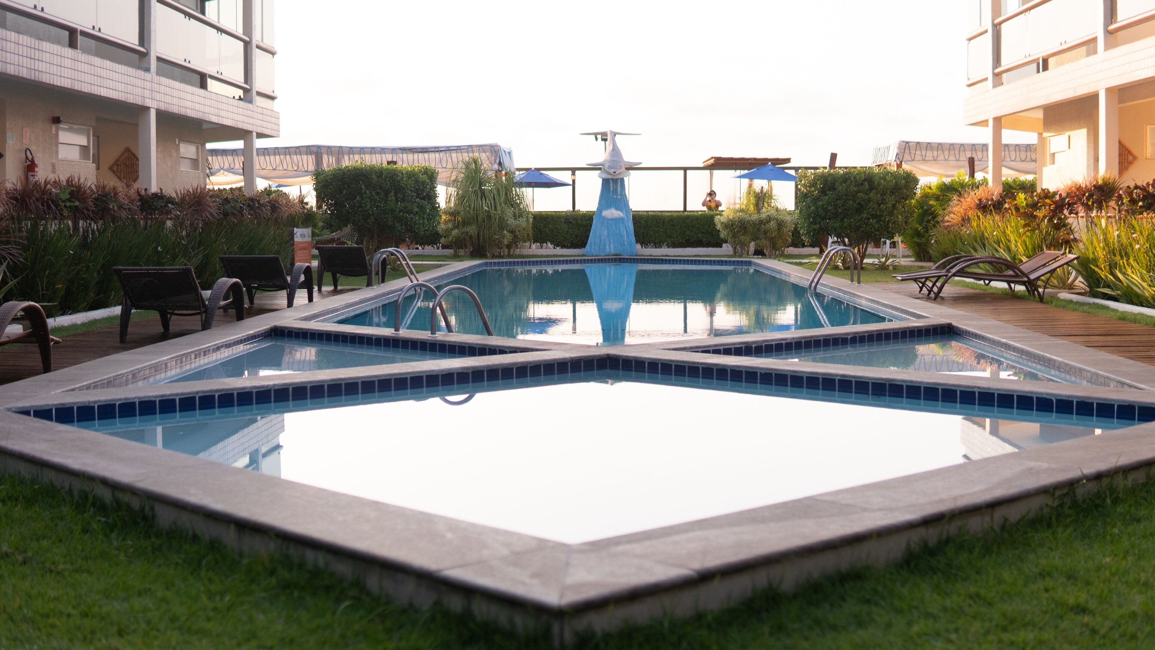 A rectangular pool with a central fountain, surrounded by lounge chairs and greenery.