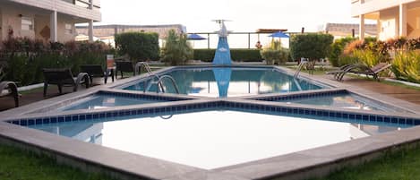 A rectangular pool with a central fountain, surrounded by lounge chairs and greenery.