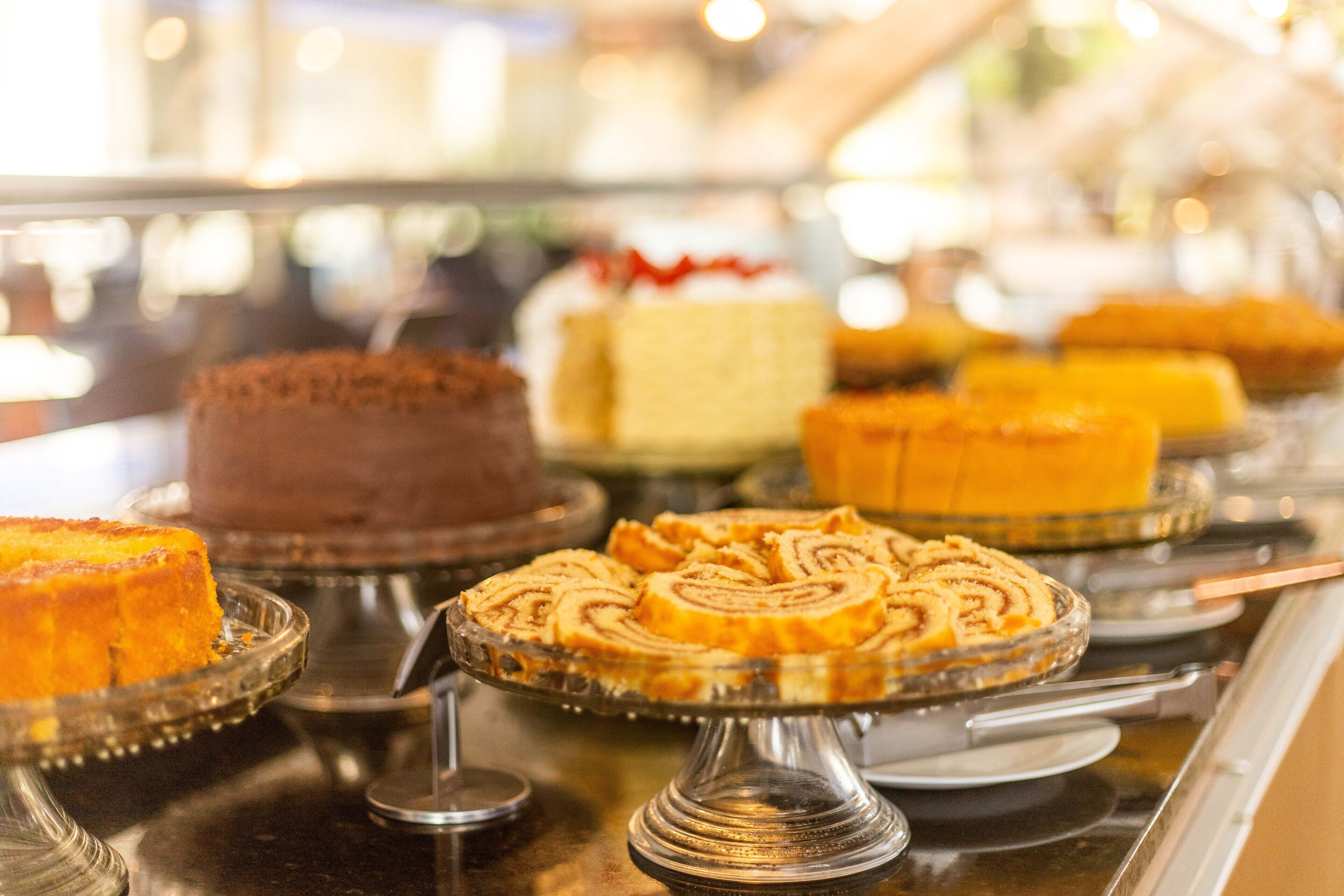 A display of various cakes on glass stands in a bakery.