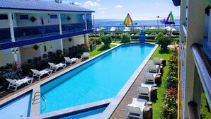 A swimming pool with lounge chairs, a view of the sea, and a building with a blue roof. - Crôa Mares Hotel (Maragogi)
