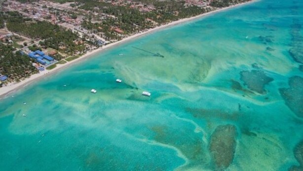 An aerial view of a coastal area with clear turquoise waters, a sandy beach, and a few boats. - Crôa Mares Hotel (Maragogi)