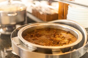 Montaje tipo bufé con una olla grande de curry y otra olla tapada al fondo.
